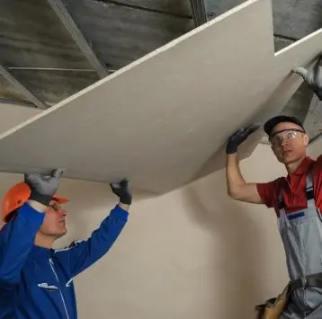 Instaladores levantando una placa de drywall para fijarla al techo