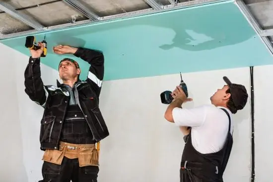 Dos instaladores atornillando una placa verde de drywall en el cielo raso, referencial para Independencia