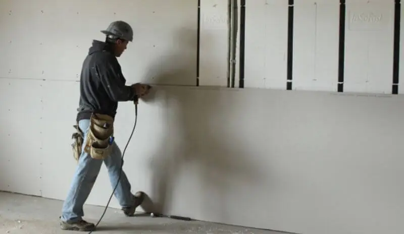 Instalador atornillando una placa de drywall a los parantes de una pared