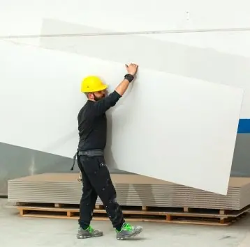 Instalador con casco cargando una placa de drywall para colocarla en la pared