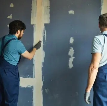 Dos operarios revisando el masillado de las juntas de una pared de drywall